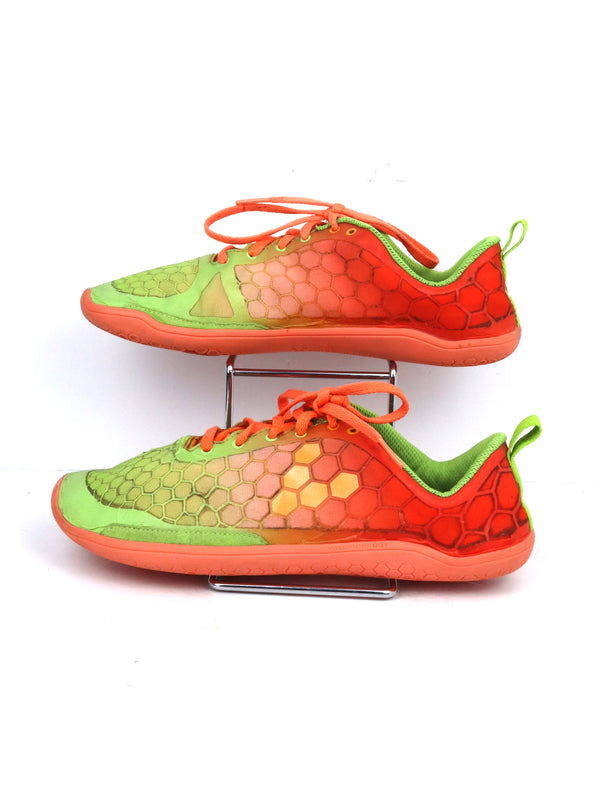 Vivobarefoot Primus Lite women's barefoot exercise shoes in an orange and lime green colorway with a hexagonal pattern.